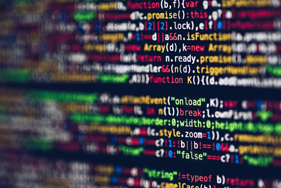 Photograph showing a close-up of a computer screen filled with lines of coloured programming code in various shades of red, green, blue, yellow, and white, displayed in a dark environment. The text ap